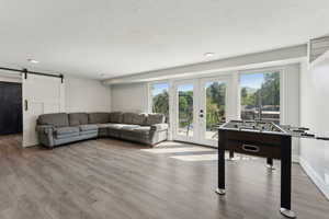 Living area featuring a barn door, french doors, wood finished floors, a textured ceiling, and recessed lighting