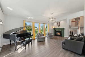 Living room with wood finished floors, a glass covered fireplace, stairway, and a chandelier