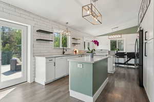 Kitchen featuring white appliances, a sink, open shelves, vaulted ceiling, and a center island