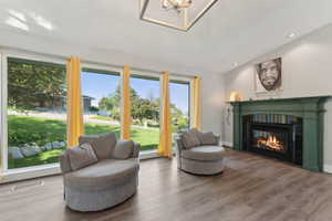 Living area featuring vaulted ceiling, a glass covered fireplace, wood finished floors, a chandelier, and recessed lighting