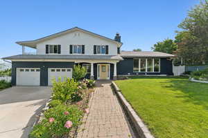 View of front of home featuring an attached garage, a chimney, concrete driveway, and brick siding