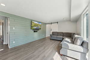 Living area featuring a barn door, wood walls, wood finished floors, recessed lighting, and baseboards
