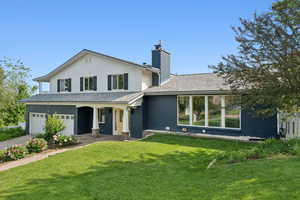 View of front facade featuring an attached garage, a front yard, a chimney, and brick siding