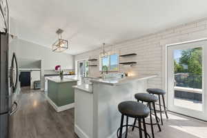 Kitchen with stainless steel fridge, dark wood-style flooring, a center island, a chandelier, and a kitchen bar