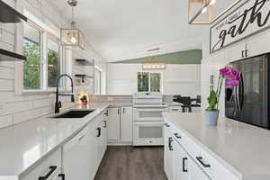 Kitchen featuring white appliances, a sink, lofted ceiling, healthy amount of natural light, and white cabinetry