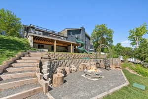 Back of property featuring a wooden deck, an outdoor fire pit, stairway, a lawn, and a patio