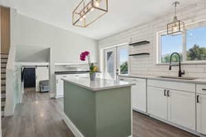 Kitchen with a sink, white dishwasher, wood finished floors, open shelves, and white cabinets