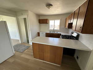 Kitchen with white appliances, a sink, a peninsula, light countertops, and light wood finished floors