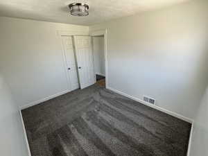 Spare room with a textured ceiling, dark carpet, and baseboards