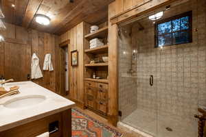 Full bath featuring a stall shower, wooden ceiling, wooden walls, and double vanity