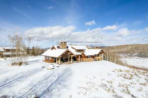 Snow covered property with a chimney and stone siding