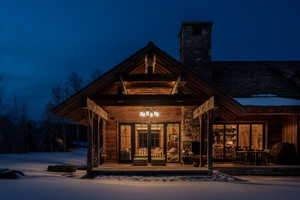 Snow covered property entrance with a chimney and stone siding