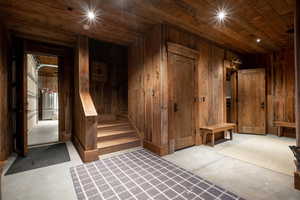 Basement with wood ceiling, wooden walls, freestanding refrigerator, and stairway