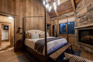 Bedroom with wood walls, high vaulted ceiling, light wood-style floors, beamed ceiling, and a stone fireplace