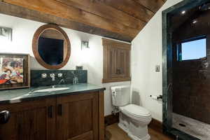 Full bath featuring toilet, tiled shower, wood finished floors, vanity, and vaulted ceiling