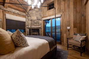 Bedroom with wooden walls, access to outside, wood finished floors, and a fireplace