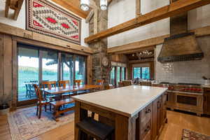 Kitchen featuring premium stove, premium range hood, a towering ceiling, light wood-type flooring, and backsplash