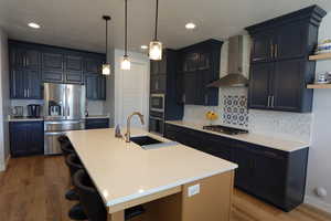Kitchen featuring appliances with stainless steel finishes, wall chimney range hood, a sink, open shelves, and a breakfast bar area