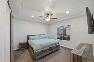 Bedroom featuring dark carpet, a tray ceiling, baseboards, recessed lighting, and ceiling fan