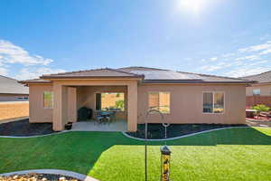 Rear view of property with a patio area, roof mounted solar panels, stucco siding, and a tiled roof
