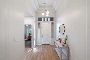Entrance foyer featuring light wood finished floors, baseboards, a chandelier, and a tray ceiling