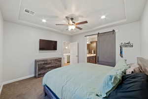 Bedroom with a raised ceiling, a barn door, baseboards, ensuite bath, and recessed lighting