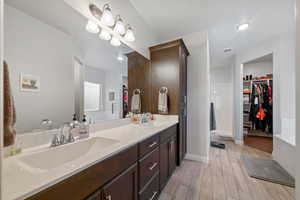 Full bathroom with double vanity, a walk in closet, wood finished floors, baseboards, and recessed lighting