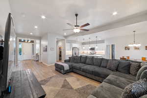 Living room with a chandelier, light wood-type flooring, a ceiling fan, recessed lighting, and baseboards