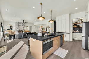 Kitchen featuring a sink, stainless steel appliances, dark countertops, ceiling fan, and a breakfast bar