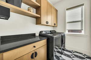 Washroom featuring washing machine and dryer, cabinet space, and baseboards