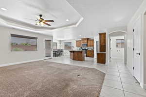 Unfurnished living room with a ceiling fan, light tile patterned floors, a textured ceiling, a raised ceiling, and baseboards