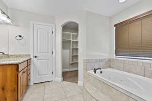 Full bathroom featuring vanity, a tub with jets, tile patterned flooring, baseboards, and a walk in closet