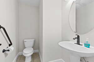 Half bathroom with toilet, a sink, baseboards, and tile patterned floors