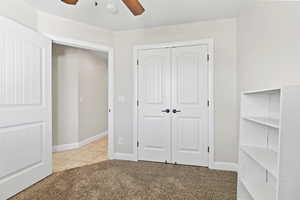 Unfurnished bedroom featuring light carpet, a closet, baseboards, a ceiling fan, and light tile patterned floors