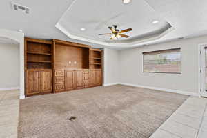 Unfurnished living room featuring a tray ceiling, a textured ceiling, a ceiling fan, baseboards, and light tile patterned flooring