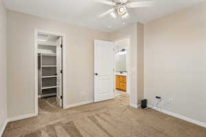Unfurnished bedroom featuring light carpet, a spacious closet, baseboards, and ceiling fan