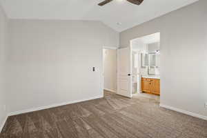Unfurnished bedroom featuring light carpet, lofted ceiling, baseboards, connected bathroom, and a ceiling fan