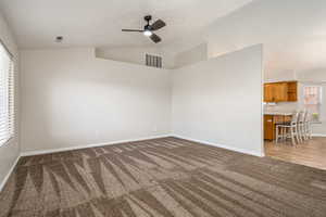 Empty room with dark colored carpet, a ceiling fan, baseboards, and lofted ceiling