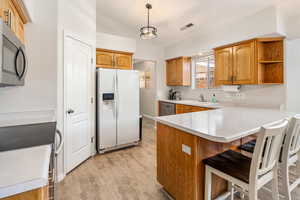 Kitchen featuring appliances with stainless steel finishes, a kitchen breakfast bar, a sink, a peninsula, and lofted ceiling