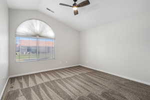Carpeted empty room featuring a ceiling fan, vaulted ceiling, and baseboards
