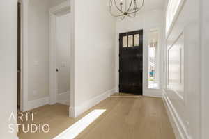 Foyer featuring light wood finished floors, a chandelier, plenty of natural light, and baseboards