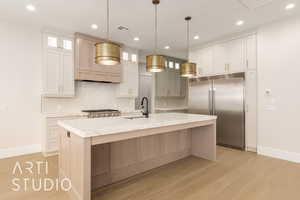 Kitchen with built in refrigerator, a sink, baseboards, tasteful backsplash, and light wood-style flooring