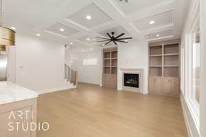 Unfurnished living room featuring coffered ceiling, light wood-style flooring, stairway, built in features, and healthy amount of natural light