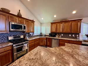 Kitchen with appliances with stainless steel finishes, vaulted ceiling, light stone countertops, tasteful backsplash, and recessed lighting