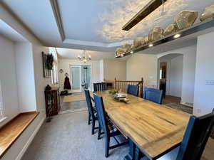 Dining space with arched walkways, a chandelier, carpet flooring, a raised ceiling, and baseboards