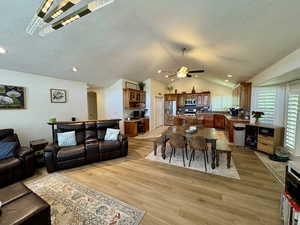 Living room featuring vaulted ceiling, ceiling fan, light wood-type flooring, a textured ceiling, and recessed lighting
