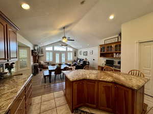 Kitchen featuring vaulted ceiling, a ceiling fan, open floor plan, a kitchen island, and light stone counters