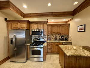 Kitchen with stainless steel appliances, a sink, crown molding, tasteful backsplash, and brown cabinets