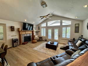 Living area featuring a textured ceiling, light wood-type flooring, lofted ceiling, a fireplace, and baseboards