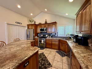 Kitchen featuring stainless steel appliances, a sink, tasteful backsplash, light stone counters, and vaulted ceiling